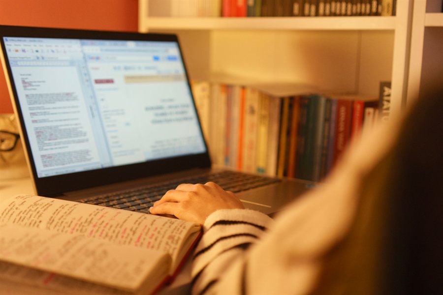 Hands on a laptop keyboard in front of a bookcase while studying online